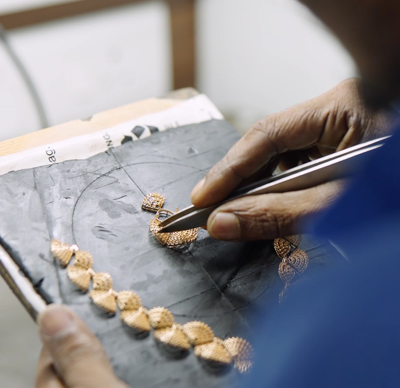 An artisan placing stones with tweezers onto a necklace on a setting board